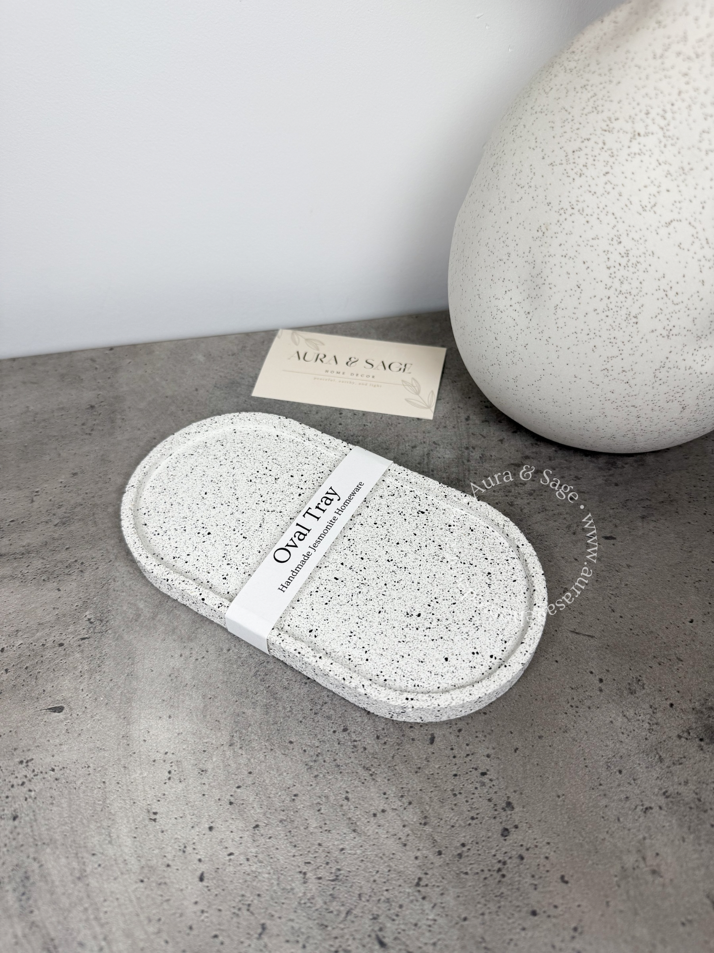 Oval speckled tray on a concrete surface with a branded card in the background