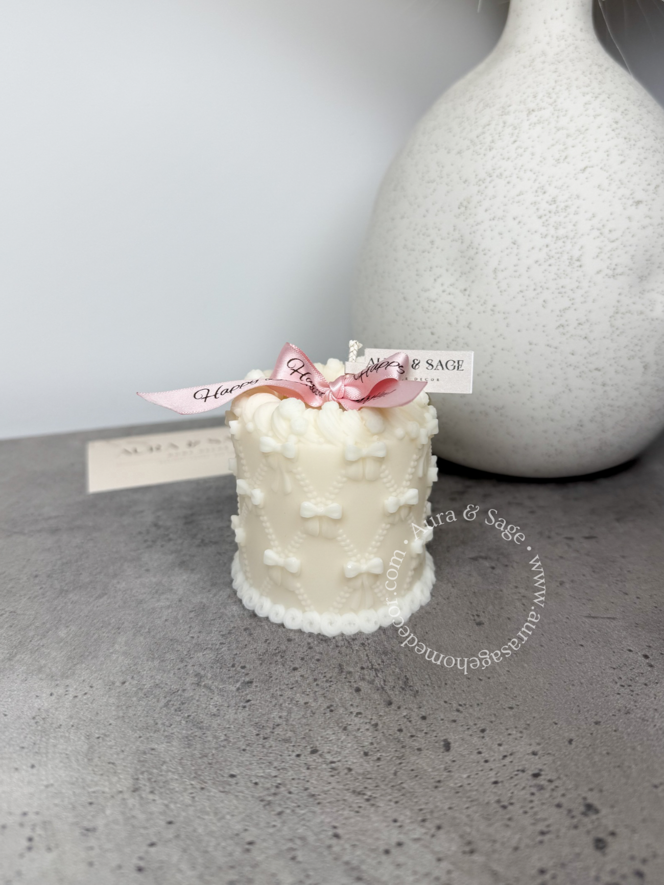Small white cake candle with pink bow on a gray surface, birthday gift.