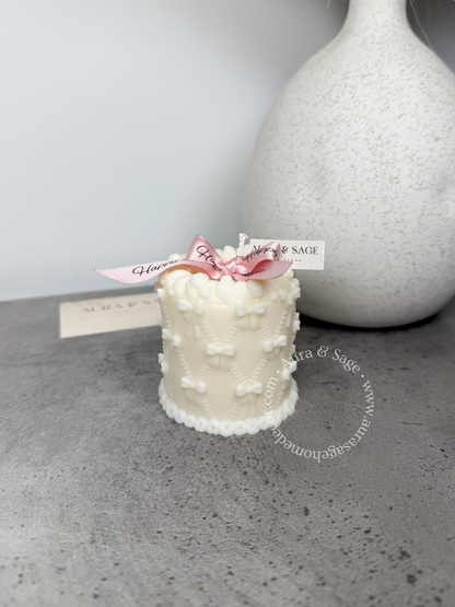 Small white cake candle with pink bow on a gray surface, birthday gift.