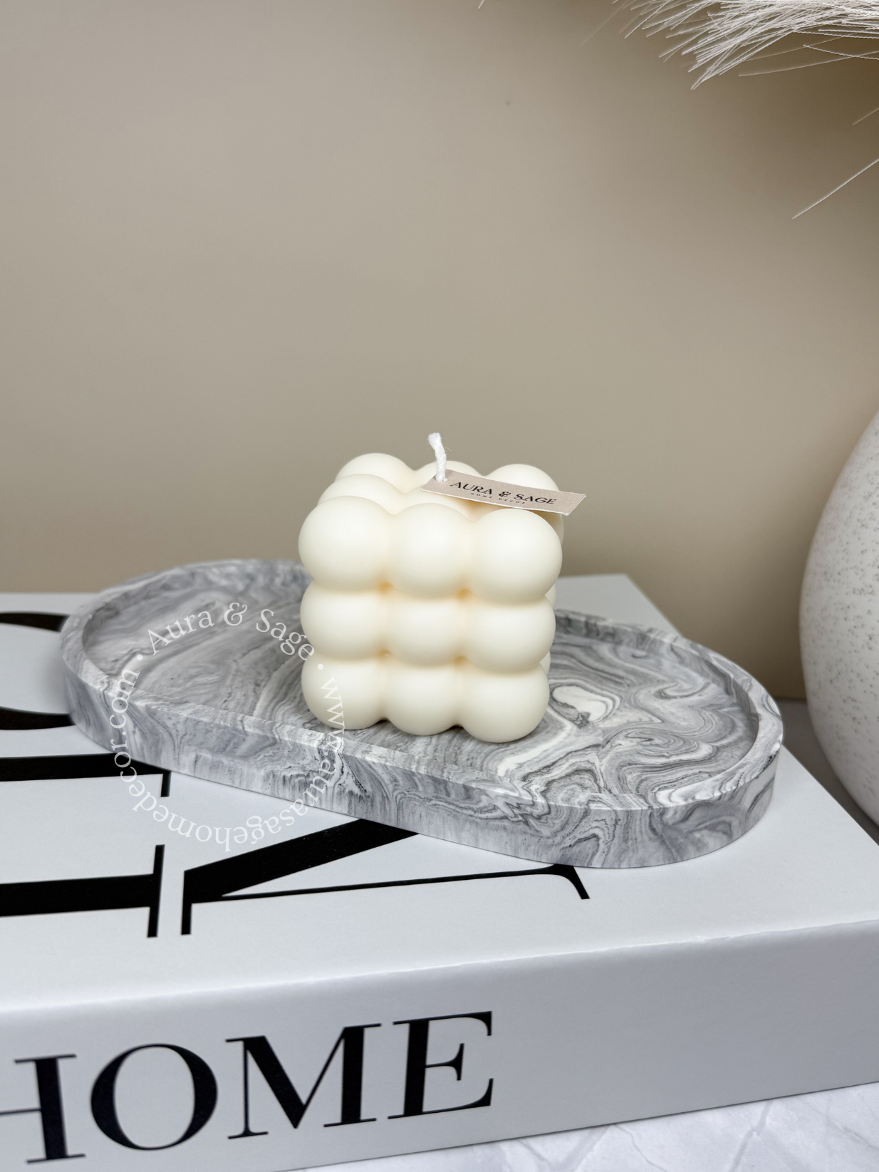 A white pillar soy candle with a bubble-like design, placed on a marble surface. 