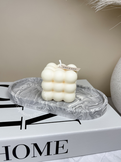 A white pillar soy candle with a bubble-like design, placed on a marble surface. 