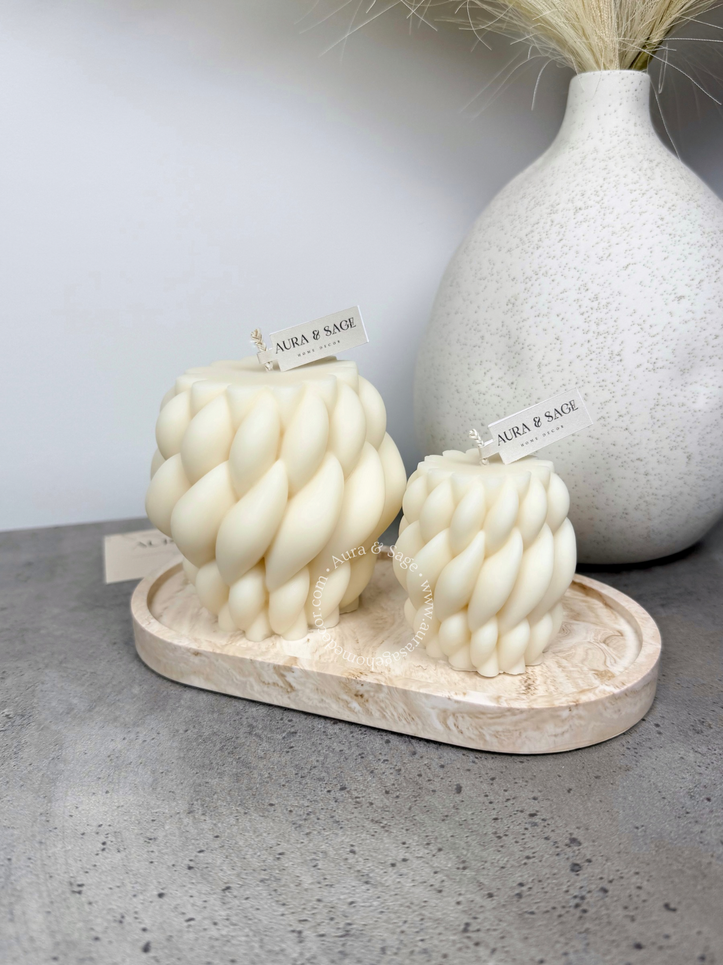 Two textured candles on a marble tray with a vase in the background